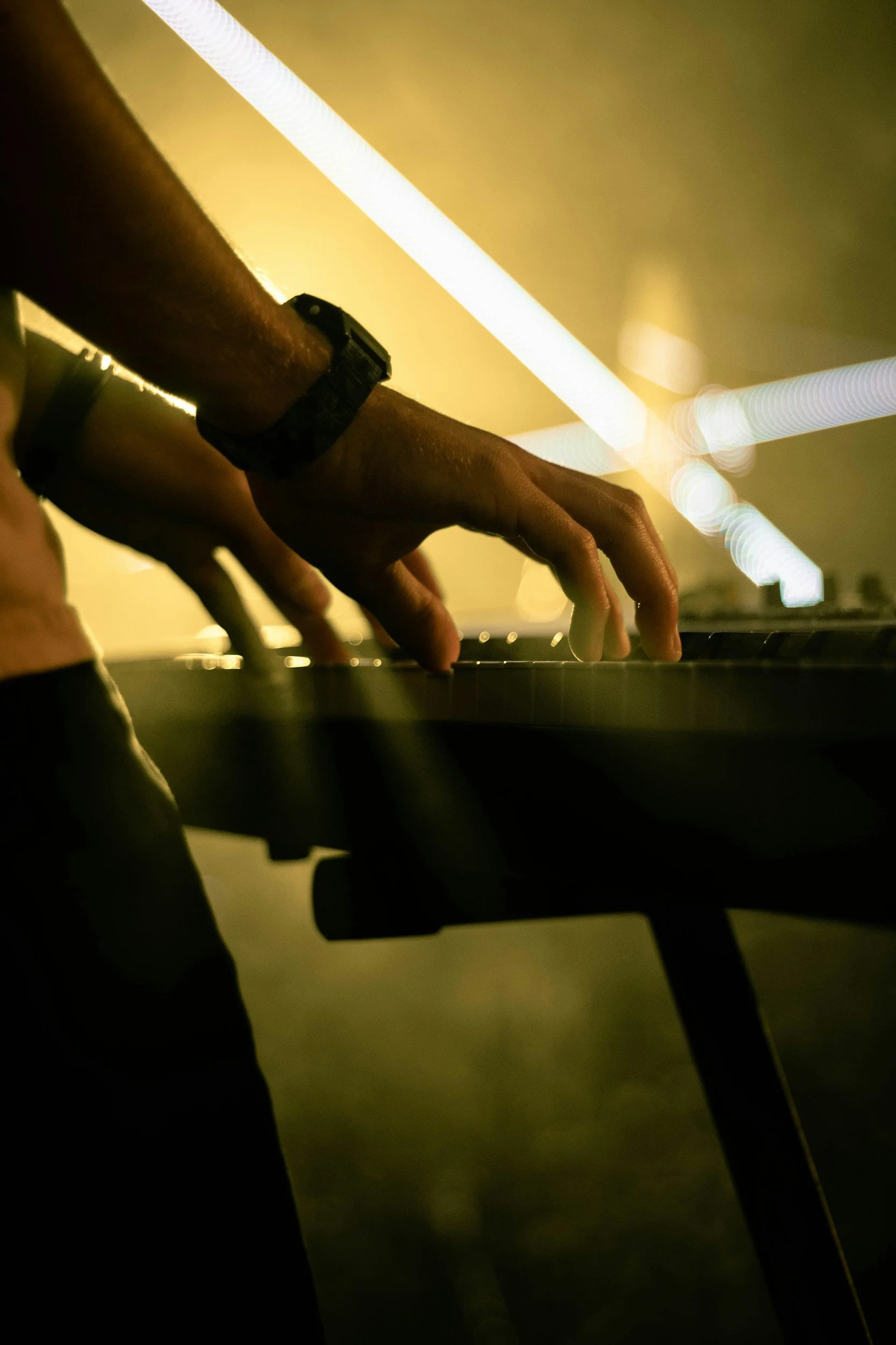 Hands playing a keyboard under stage lights